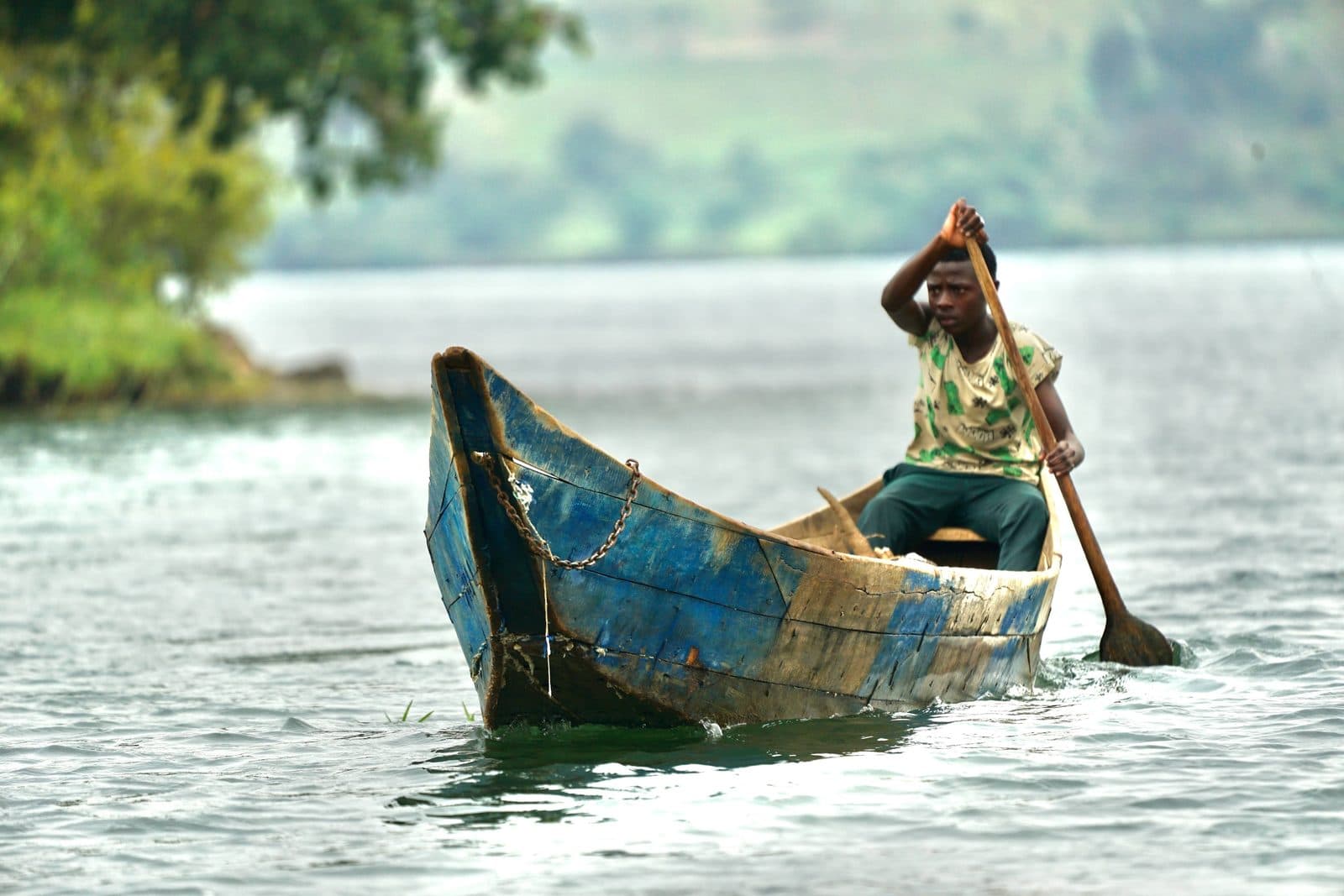 A fisherman standing in a wooden canoe on the still water at dawn